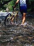 Backview of Cyclist Walking Bicycle Through Stream