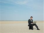 Businessman sitting on a briefcase in the desert