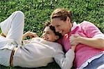 Mother and daughter reclining in grass, laughing, holding hands