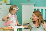 Little girl playing in bedroom with mother, pretending to iron