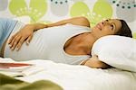 Femme enceinte allongée sur le lit, le sourire aux lèvres, regardant vers le haut