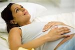 Pregnant woman lying on back with hands on stomach, looking up and smiling