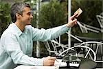 Man sitting in outdoor cafe, holding out credit card to pay