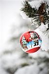 Colorful Christmas ornament hanging from snow-covered branch