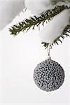 Silver Christmas ornament hanging from snow-covered evergreen branch