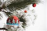 Colorful Christmas ornaments hanging from snow-covered evergreen branches