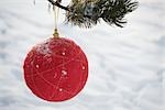 Red Christmas ornament hanging from evergreen branch, snow in background