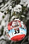 Colorful Christmas ornament hanging from snow frosted branch