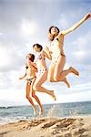 Three young women in bikinis jumping on the beach
