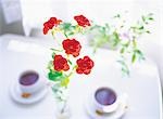 Rote Rose mit zwei Tassen Tee im Hintergrund