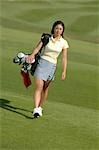 Young Asian female walking across course with golf bag