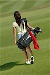 Rear view of young female golfer walking across course