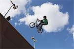 Man jumping with bicycle against cloudy sky