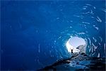 Silhouetted figure holding ice axes in each upraised arm, stands near the entrance of an ice cave at Mendenhall Glacier near Juneau. Summer in Southeast Alaska.