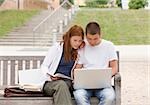Teenage couple with books and laptop on bench