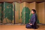 Young man in kimono sitting in front of folding screen