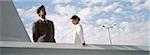 Businessman and businesswoman standing on rooftop, man looking at view, woman looking down