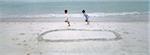Boys running on beach, chasing each other around circle drawn in sand