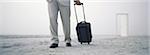 Man walking with rolling luggage on beach, open door in distance