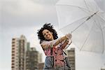 Junge Frau festhalten Regenschirm an windigen Tag, lachen