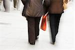 Pedestrians walking on sidewalk, one carrying shopping bag, rear view