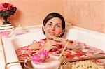 Woman in bath tub with petals holding a flower