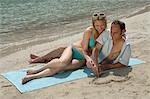 Couple sur la plage située sur une serviette, il peint un coeur dans le sable