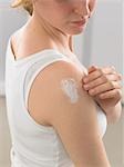 Woman is putting lotion on her shoulder