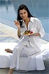 Femme vêtue de blanc manger salade à la piscine