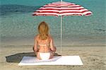 Femme assise sur la plage sous un parasol - retour vue