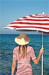 Femme portant un chapeau et un rouge et blanc parasol dans l'eau