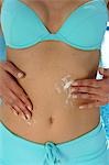 Woman in a turquoise bikini is applying sunlotion on her belly