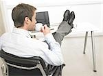 Business man with feet on desk is drinking coffee