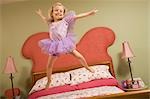 Petite fille habillée comme fée sautant sur le lit