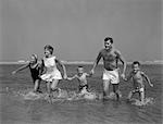 1960s FAMILY HOLDING HANDS RUNNING IN WATER AT OCEAN BEACH