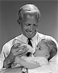 1960s SMILING FATHER FEEDING CHILD MILK IN BABY BOTTLE