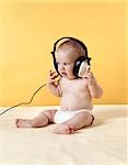 1970s BABY WEARING DIAPER LISTENING TO OVERSIZED HEADPHONES YELLOW BACKGROUND