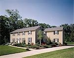 1970s TWO STORY COLONIAL TAN HOUSE WITH BLACK SHUTTERS LANDSCAPED LAWN