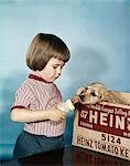 1950s 1960s SERIOUS LITTLE GIRL TRYING TO FEED COCKER SPANIEL SITTING IN HEINZ KETCHUP BOX A BABY BOTTLE OF MILK STUDIO