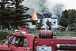 INCENDIE DE LA MAISON RURALE AVEC BÉNÉVOLE CAMION DE POMPIER EN PREMIER PLAN