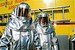 TWO PEOPLE IN SILVER FIRE FIGHTING SUITS