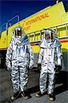 TWO PEOPLE IN SILVER FIRE FIGHTING SUITS