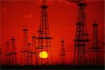 OIL FIELD DERRICKS SILHOUETTED AGAINST RED SKY AND YELLOW SUN