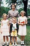 ANNÉES 1950 MÈRE ET SES TROIS ENFANTS TOUS DÉGUISÉS POSANT POUR LA PHOTO EN PLEIN AIR