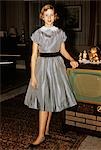 1950s TEENAGE GIRL DRESSED FOR HER FIRST DATE IN GRAY SILKY DRESS POSED BY TELEVISION SET