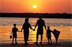 FAMILY AT THE BEACH AT SUNSET HOLDING A KITE