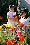 HISPANIC MOTHER AND DAUGHTER PICKING FLOWERS IN GARDEN