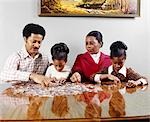 1970s AFRICAN AMERICAN FAMILY SITTING AT TABLE DOING JIGSAW PUZZLE