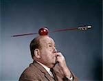 1960s ANXIOUS BUSINESS MAN BITING FINGER WITH NAILS ARROW SHOT THROUGH APPLE ON OF HIS TOP HEAD