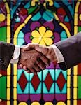 1960s AFRICAN AMERICAN AND CAUCASIAN MALE HANDSHAKE IN FRONT OF STAINED GLASS WINDOW